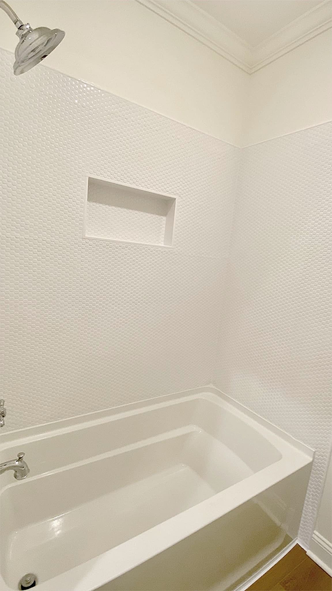 White tiled shower with built-in shelf and bathtub; chrome showerhead and faucet.