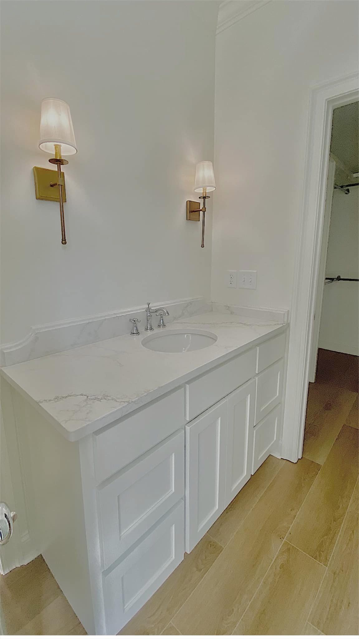 White bathroom vanity with marble countertop and gold sconces; next to a doorway.