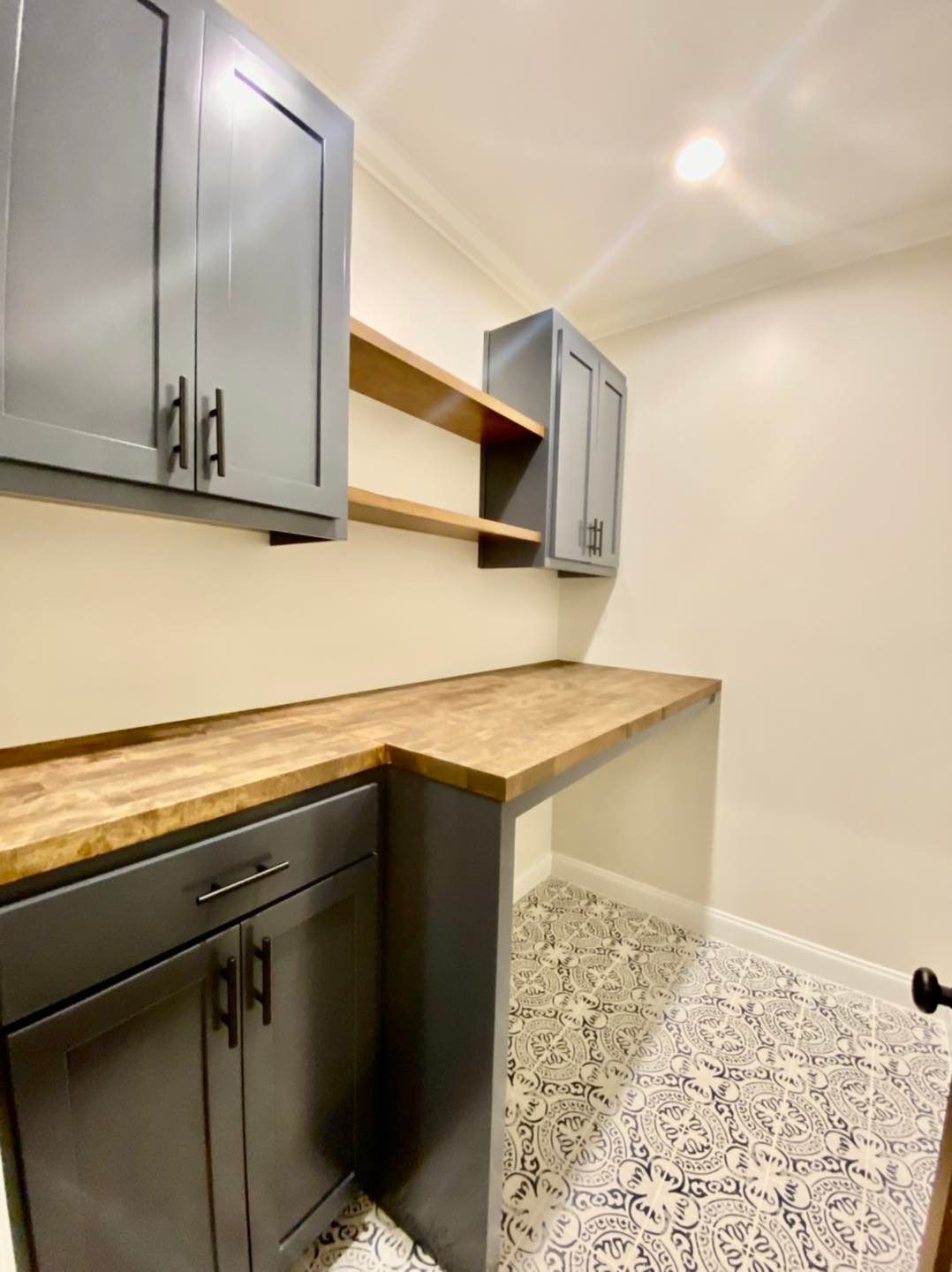 Laundry room with gray cabinets, wooden countertop, and patterned tile floor.