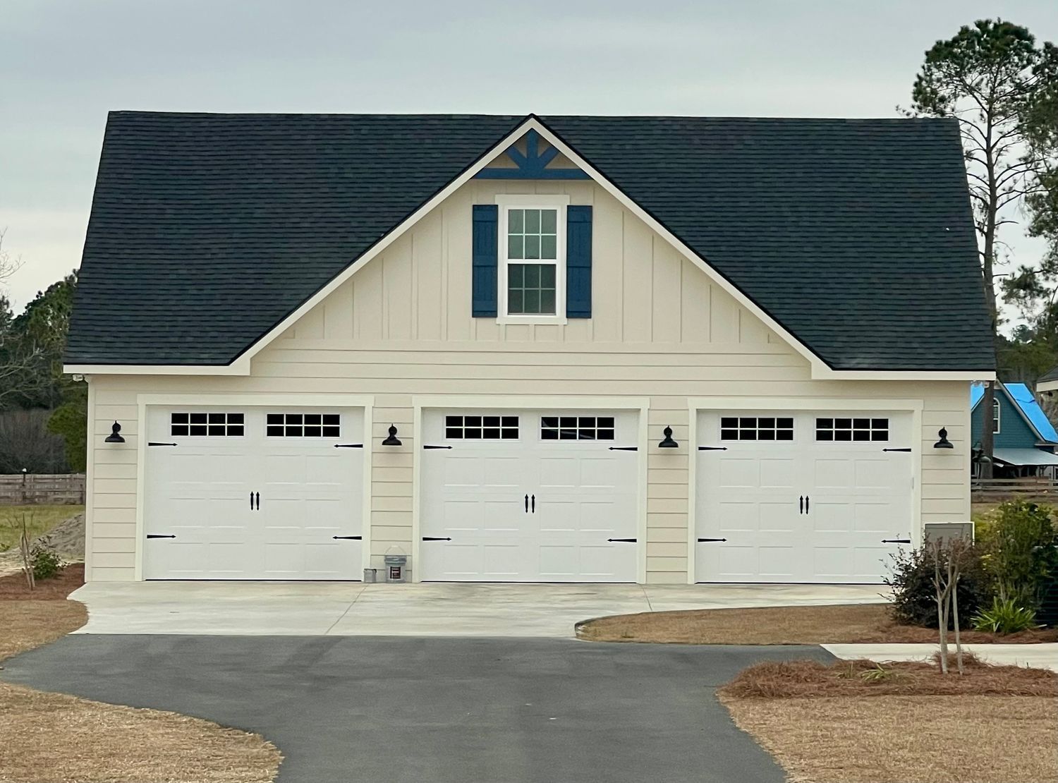 Three-bay garage with white doors and a dark roof. A blue shuttered window is centered in the gable.