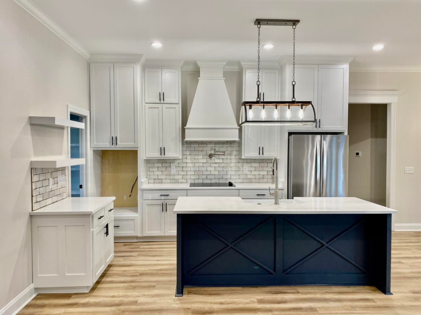 Modern kitchen with white cabinets, dark blue island, stainless steel appliances, and light wood flooring.