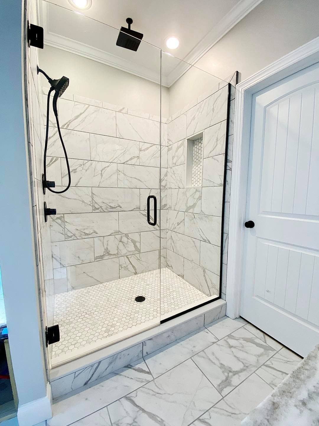 Modern marble-tiled shower with black fixtures and glass door. White door to the right.
