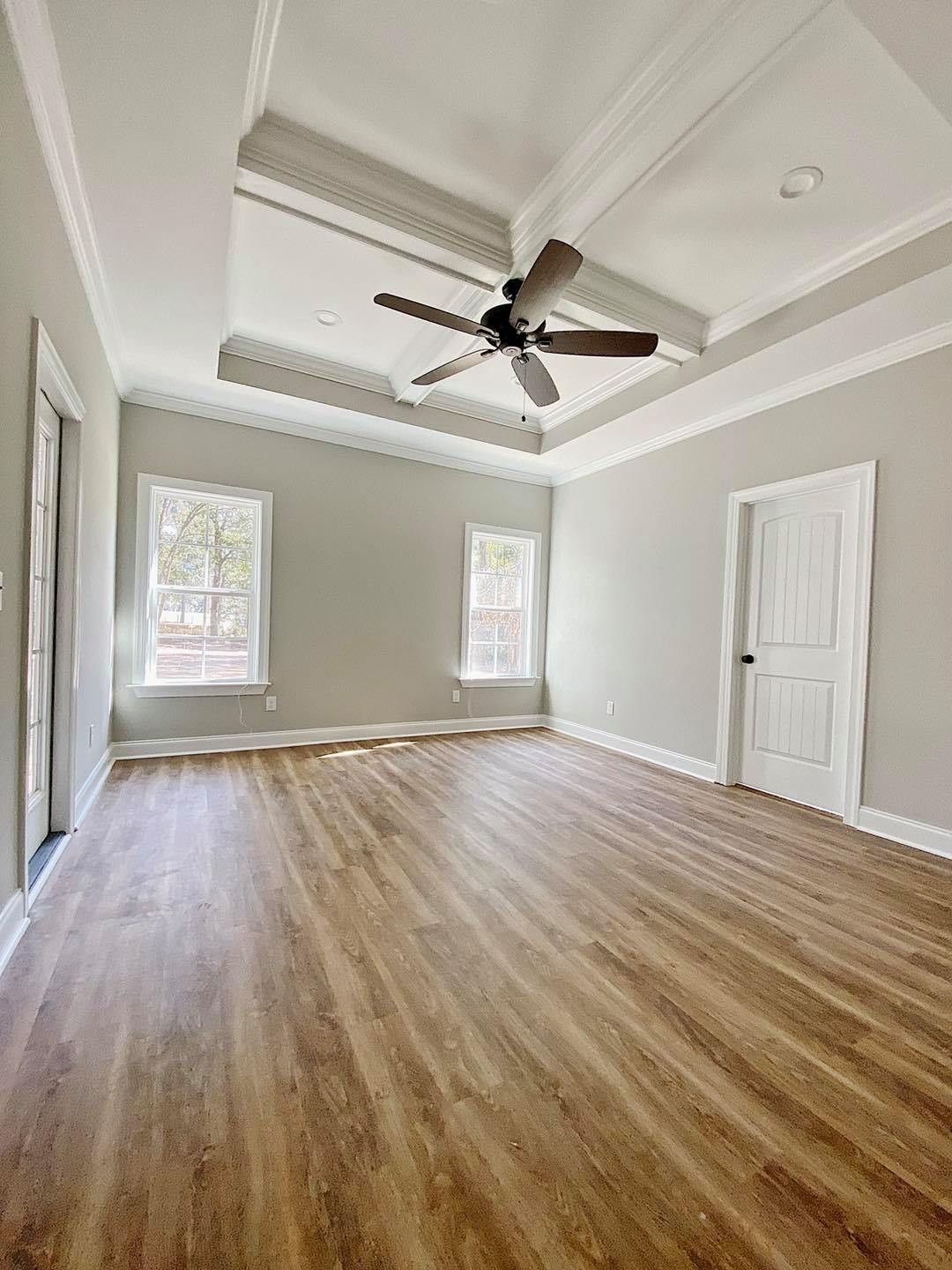 Empty bedroom with hardwood floors, light gray walls, two windows, a white door, and a ceiling fan.
