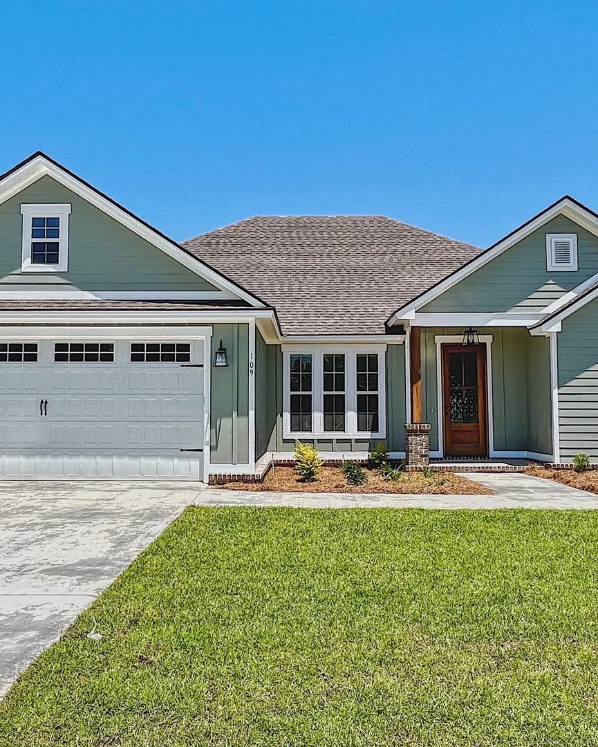 Green and gray house with a brown door and a green lawn under a blue sky.