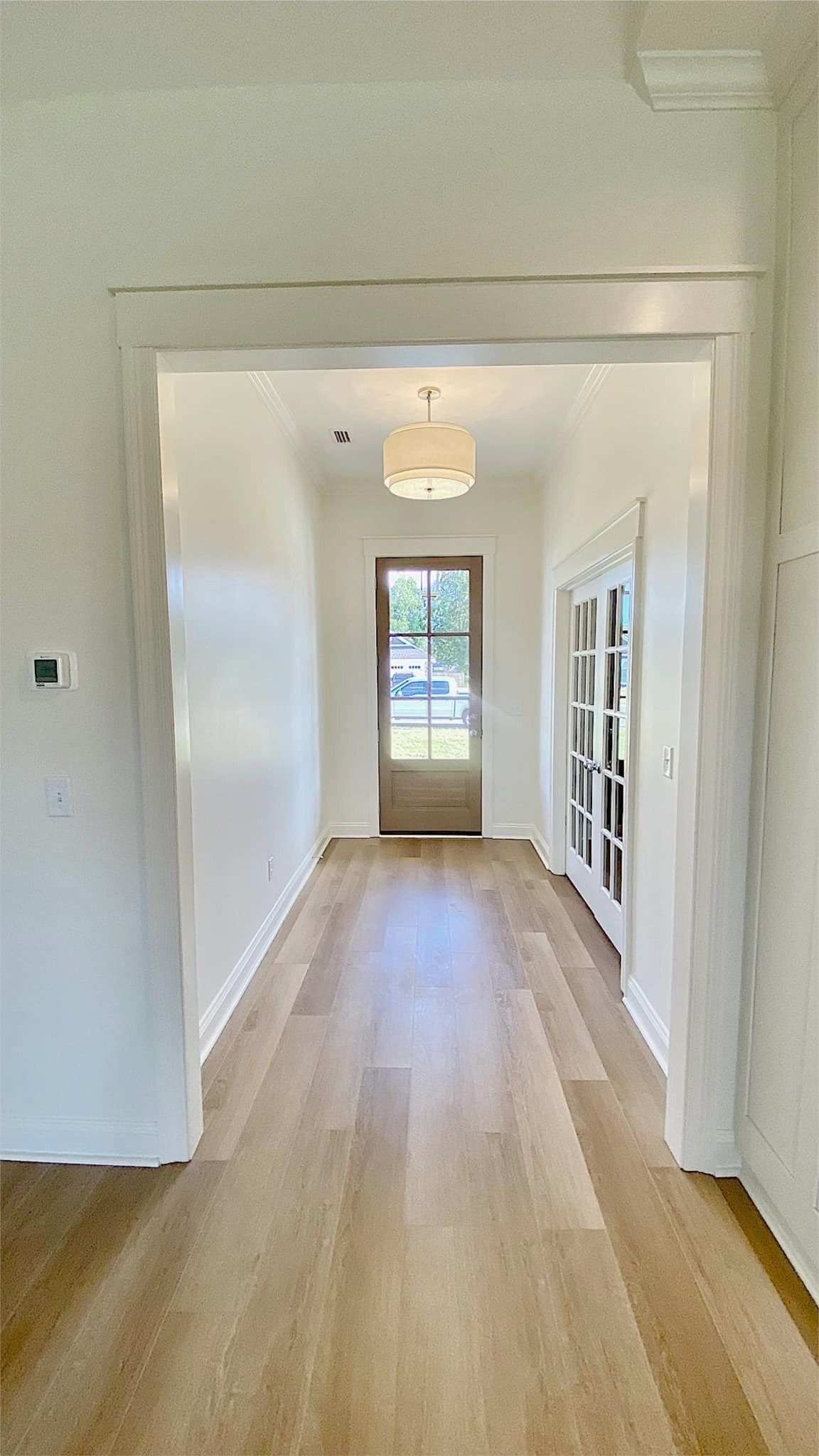 Hallway with light wood floors, white walls, and a light fixture, leading to an exterior door.