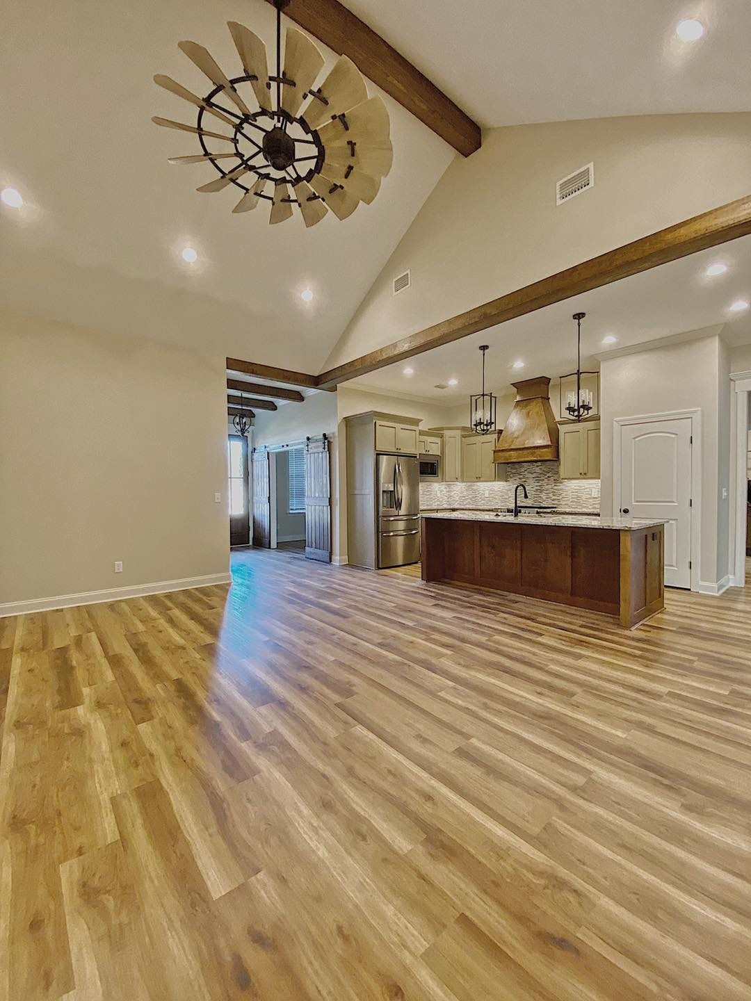 Spacious open-concept kitchen and living area with wood floors, exposed beams, and a large ceiling fan.