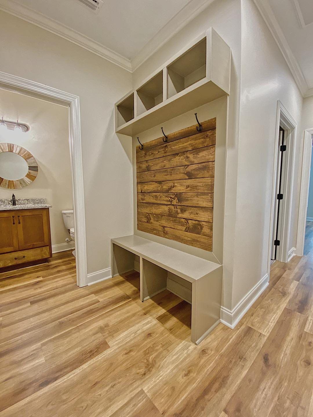 Hallway with built-in bench and storage cubbies. Wooden accent on the wall. Light colored walls and flooring.