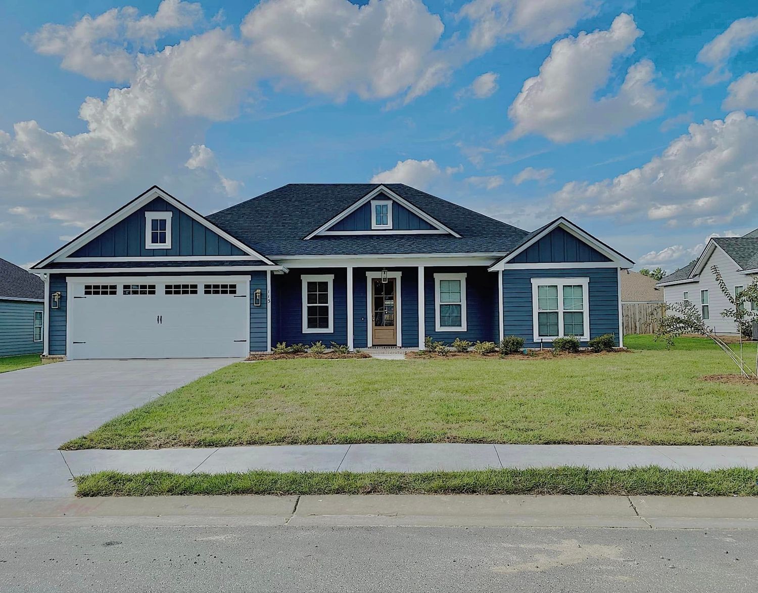 Blue house with white trim, green lawn, driveway, and blue sky.