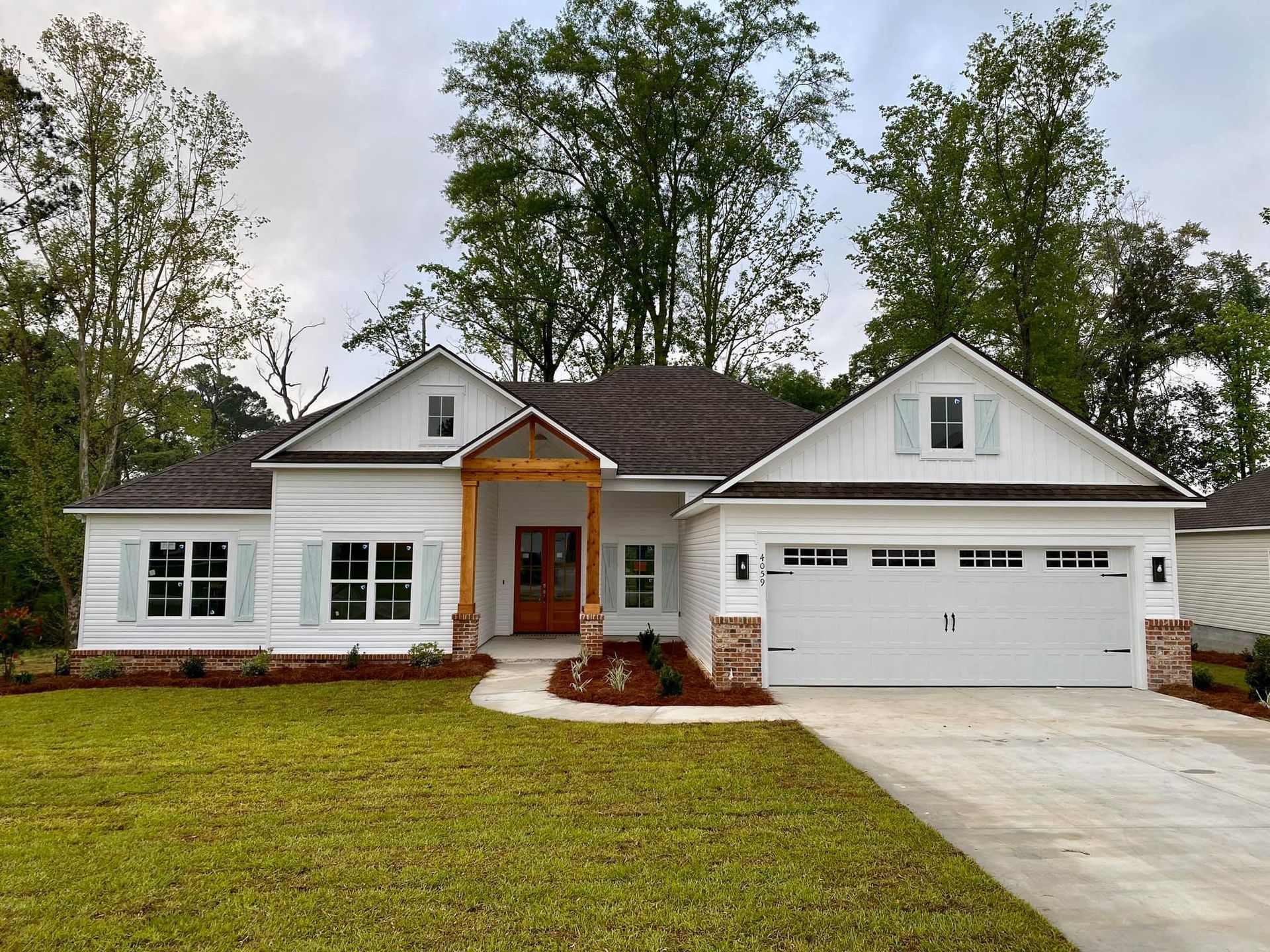 White house with brown roof, light blue shutters, brick accents, and a concrete driveway.