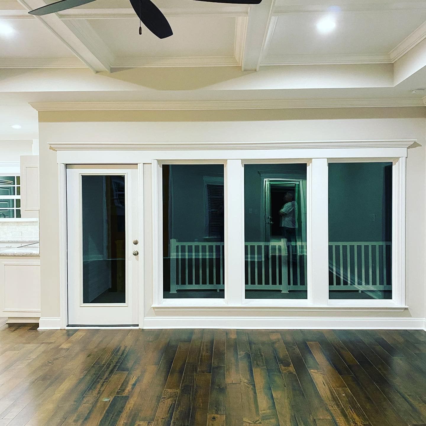 Interior view of a room with a door and three windows, a white railing is visible behind the glass.