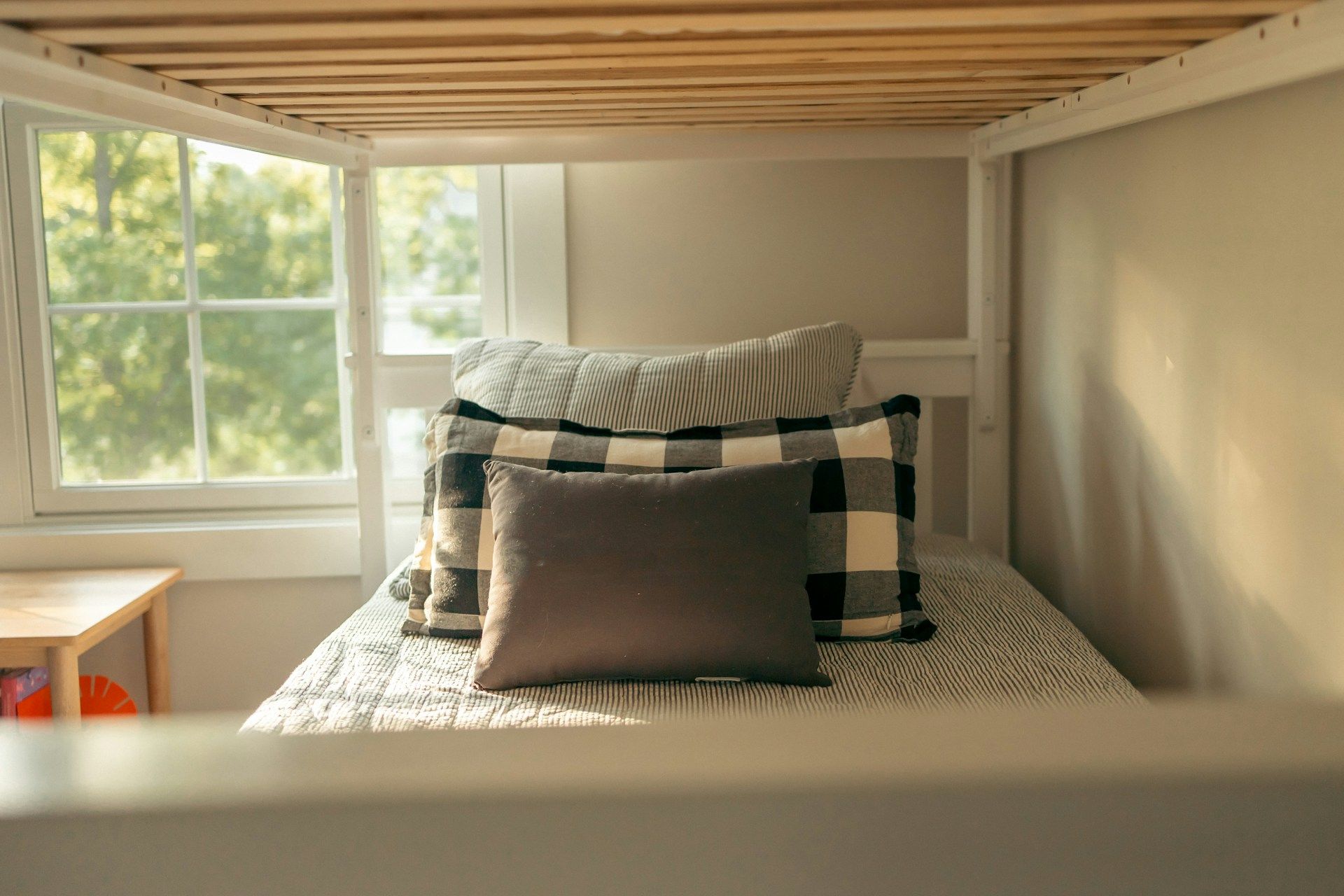 Bed with pillows under a white bunk bed, near a window.