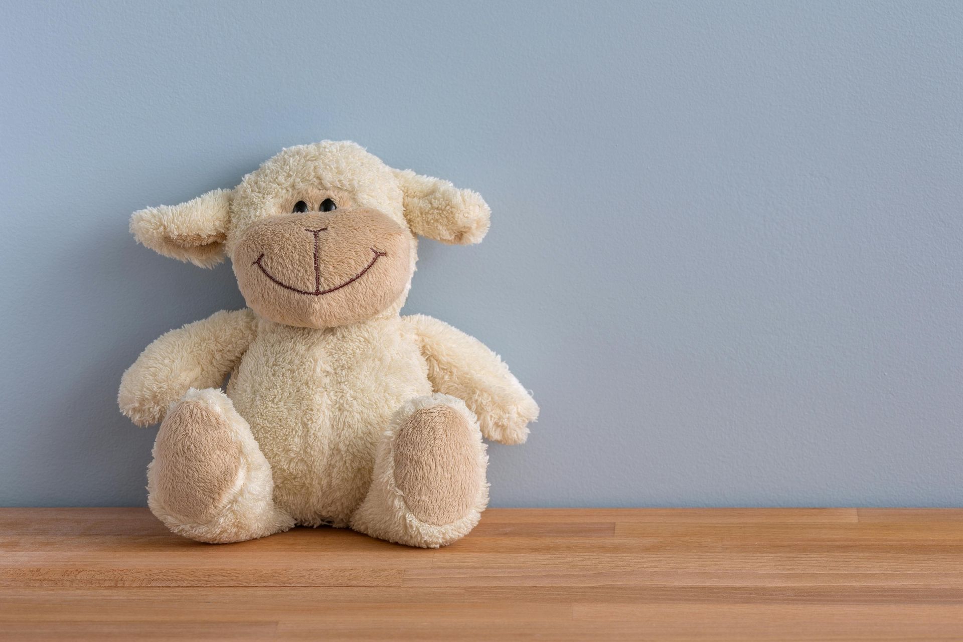 A stuffed sheep is sitting on a wooden table.