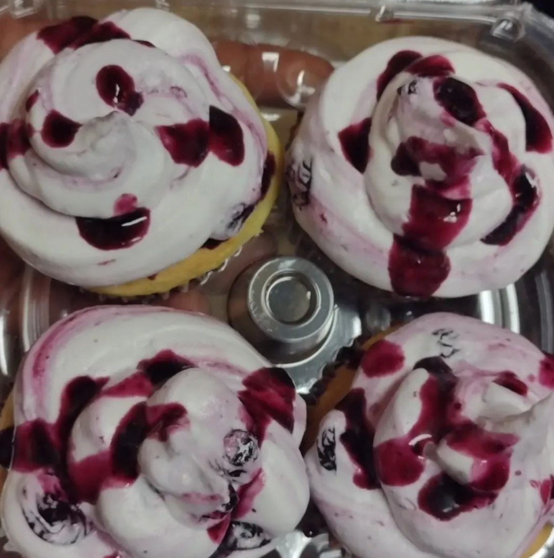Four cupcakes with white frosting and berry sauce on them