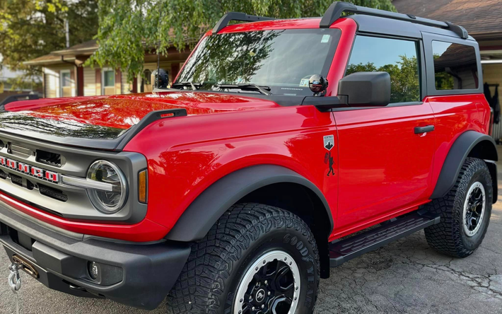 a red ford bronco is parked in front of a house .