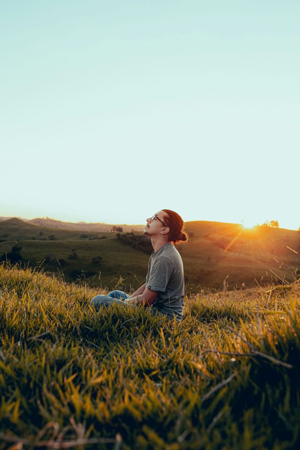 Man seated on field of grass with sunset in the background