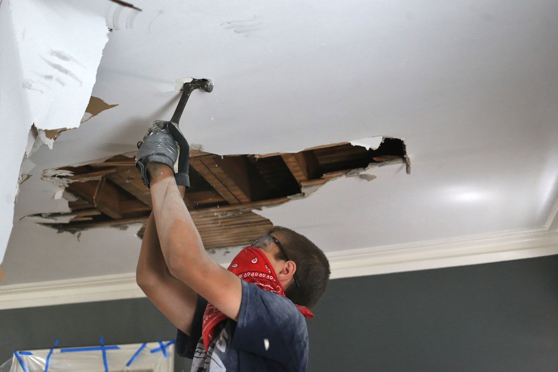 A man is hammering a hole in the ceiling with a hammer.