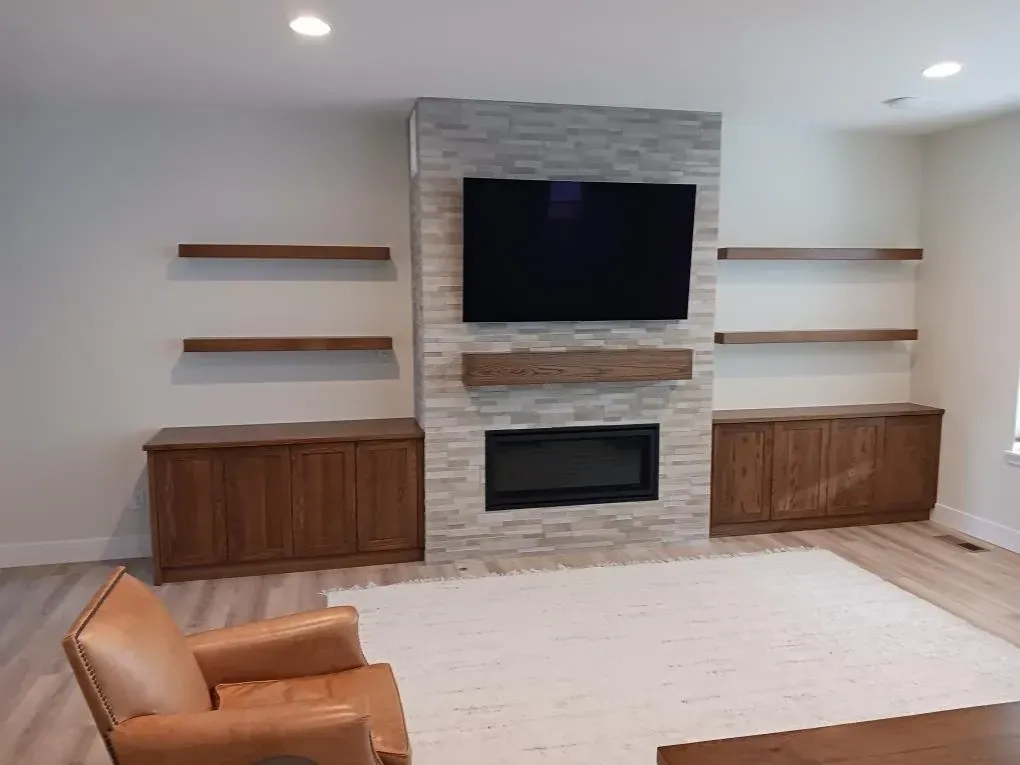 Modern living room with wall-mounted TV, fireplace, wood cabinets, and beige seating around a large rug