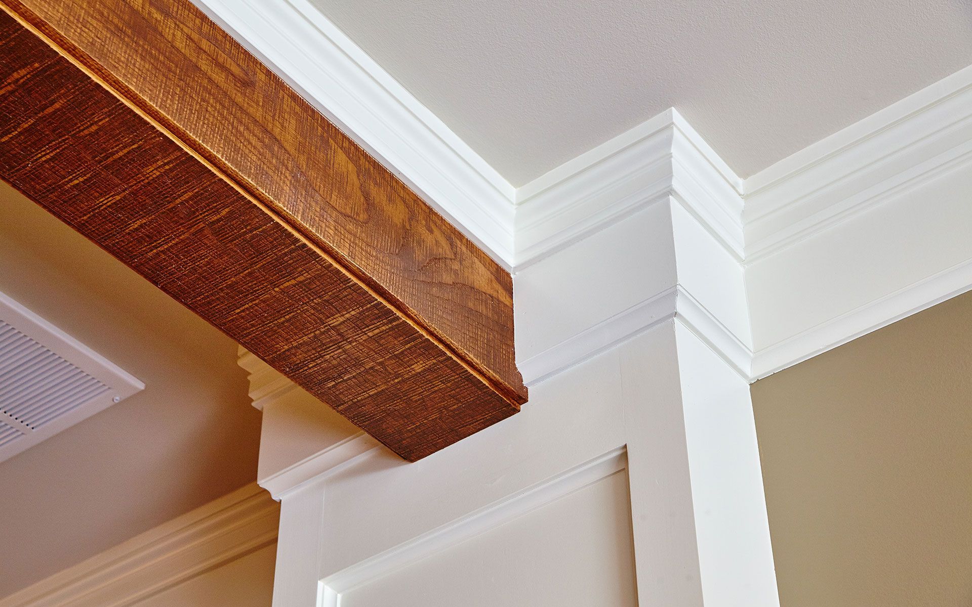 Wooden beam intersecting with white trim and a beige wall.