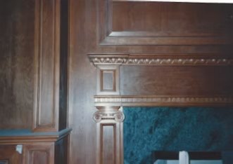 Wooden paneling with ornate trim, framing a dark green marble fireplace.