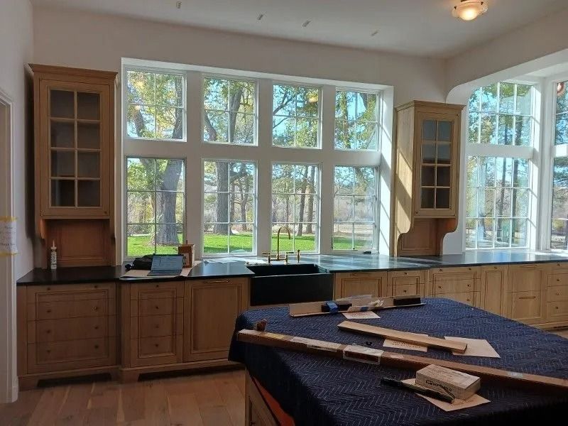 Kitchen with large windows, light wood cabinets, black countertops, and a dark blue island.