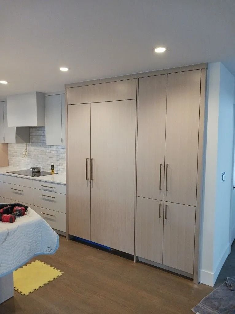 A light-colored kitchen with a large refrigerator and cabinetry against a wall. Hardwood flooring is in view.