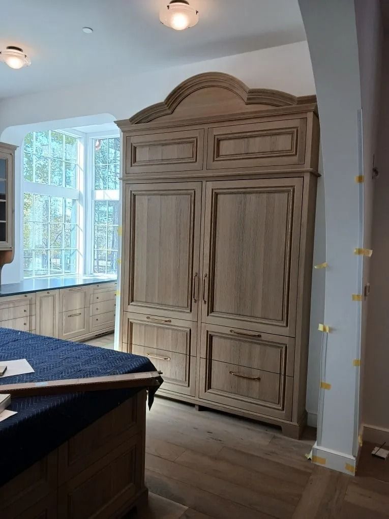 Wooden cabinet with arched top in kitchen, window in background.