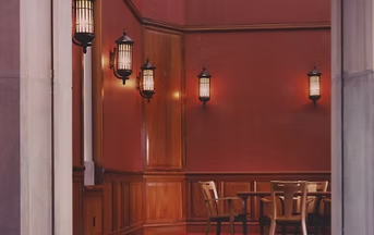 Red-walled room with wooden paneling, sconce lights, and a table with chairs. Viewed through an opening.