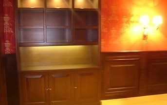 Dark wood cabinet with glass shelves, lit from within, against a red and dark wood paneled wall.