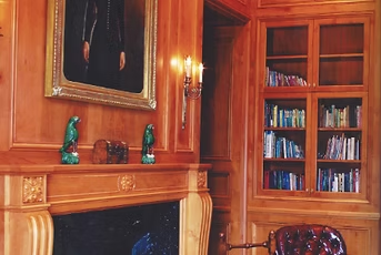 Wooden paneled library with fireplace, bookshelves, and art.
