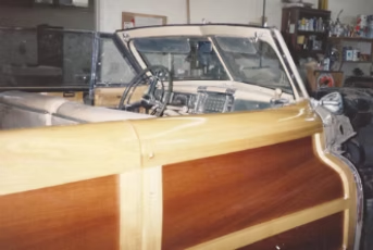 Classic wood-paneled convertible car in a garage with open doors and a partially visible interior.