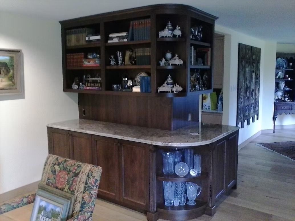 Dark wood built-in cabinet with marble countertop and upper shelving filled with decorative items.
