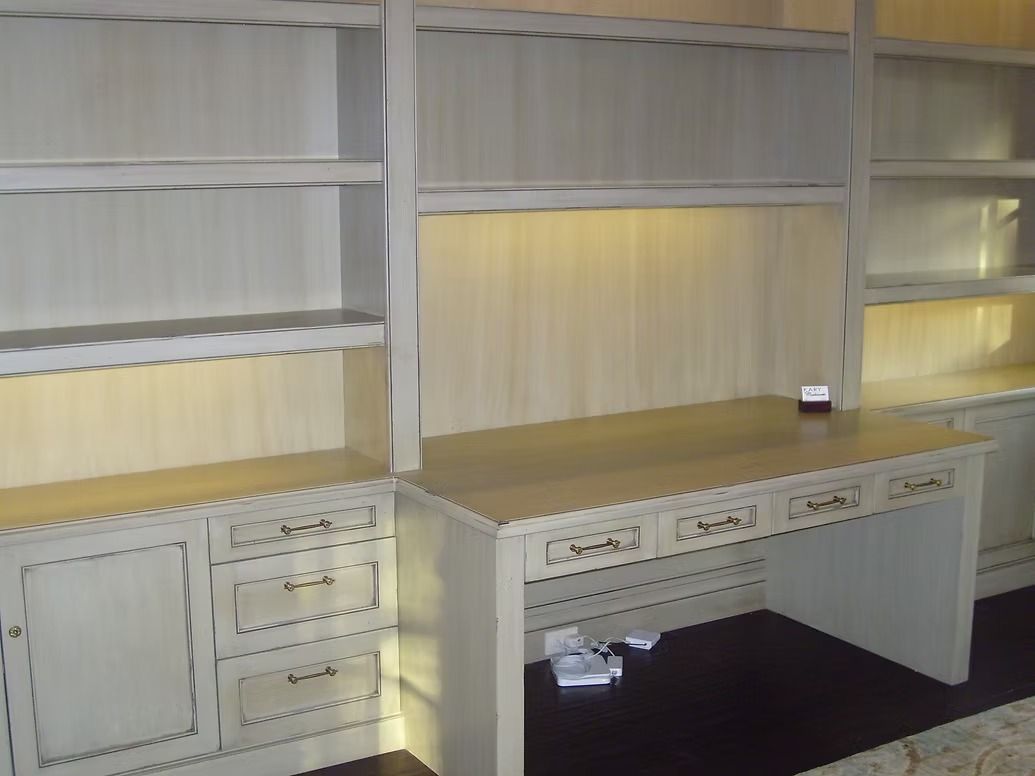 Built-in wooden desk and shelves, painted off-white, with drawers and storage. Beige background.