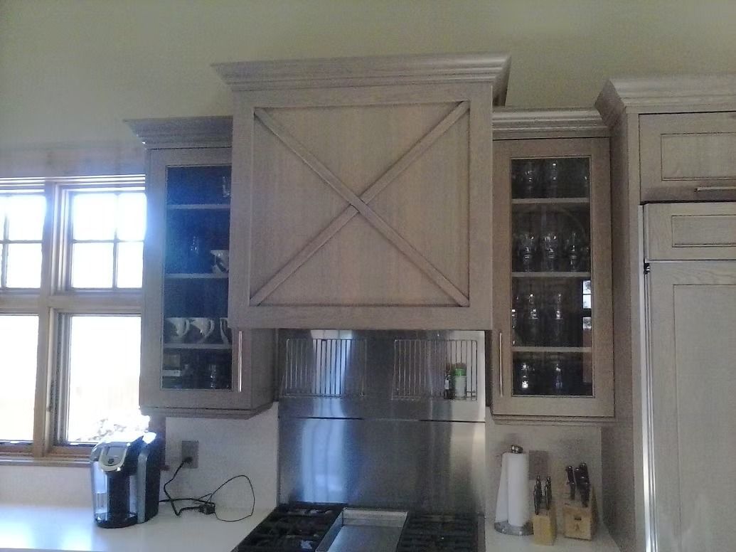 Kitchen with light-colored cabinets. Stainless steel range hood above the stovetop. Window in the background.