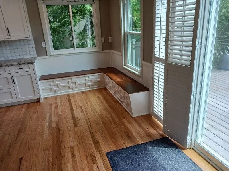 Kitchen with hardwood floors, built-in bench seating, large windows, and white cabinetry.