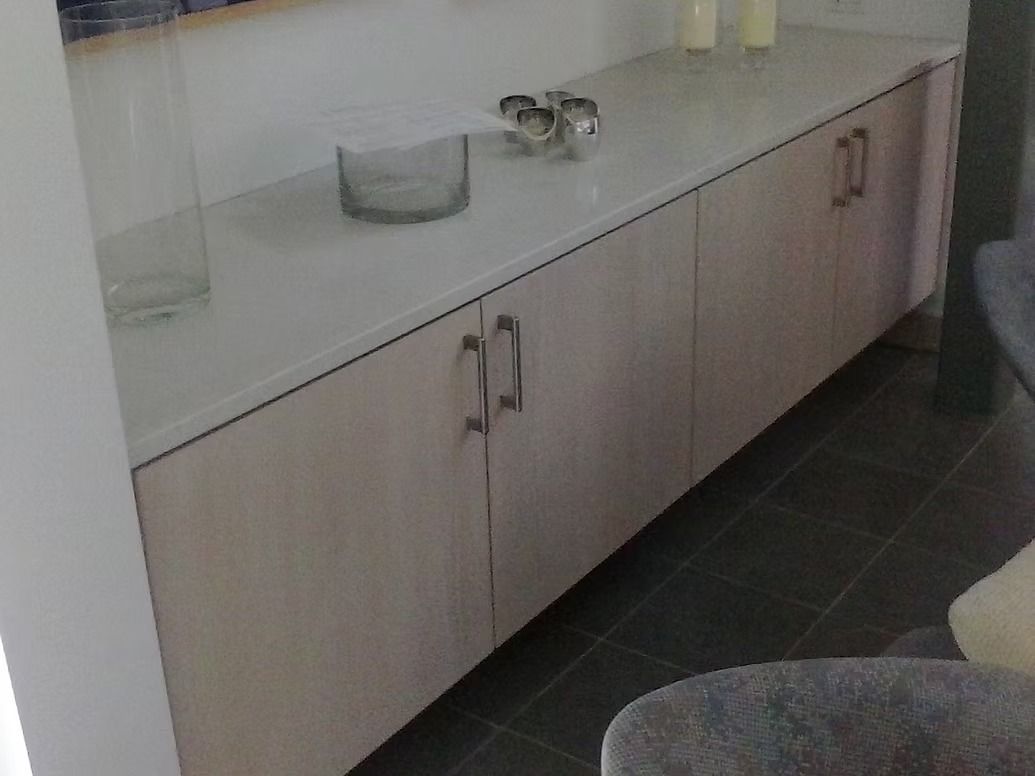 Long, light-colored cabinet with a white countertop and dark tile floor. Decorative objects are on top.