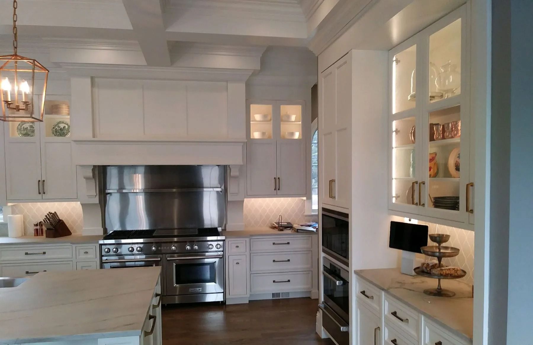 White kitchen with stainless steel appliances, marble countertops, and glass-front cabinets.