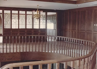 Wooden paneled room with curved railing and ornate chandelier.