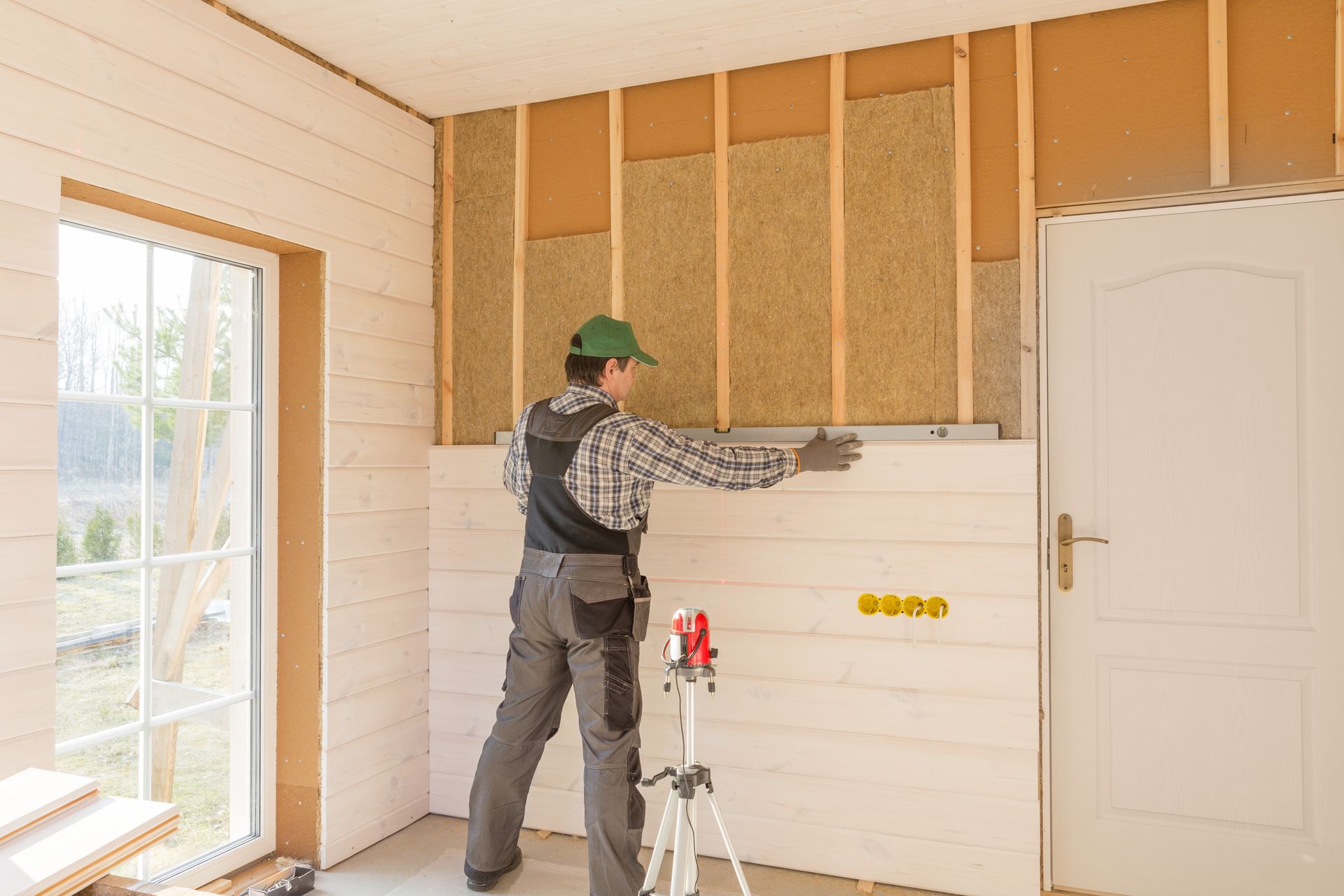 Construction worker installing paneling on an interior wall with insulation.