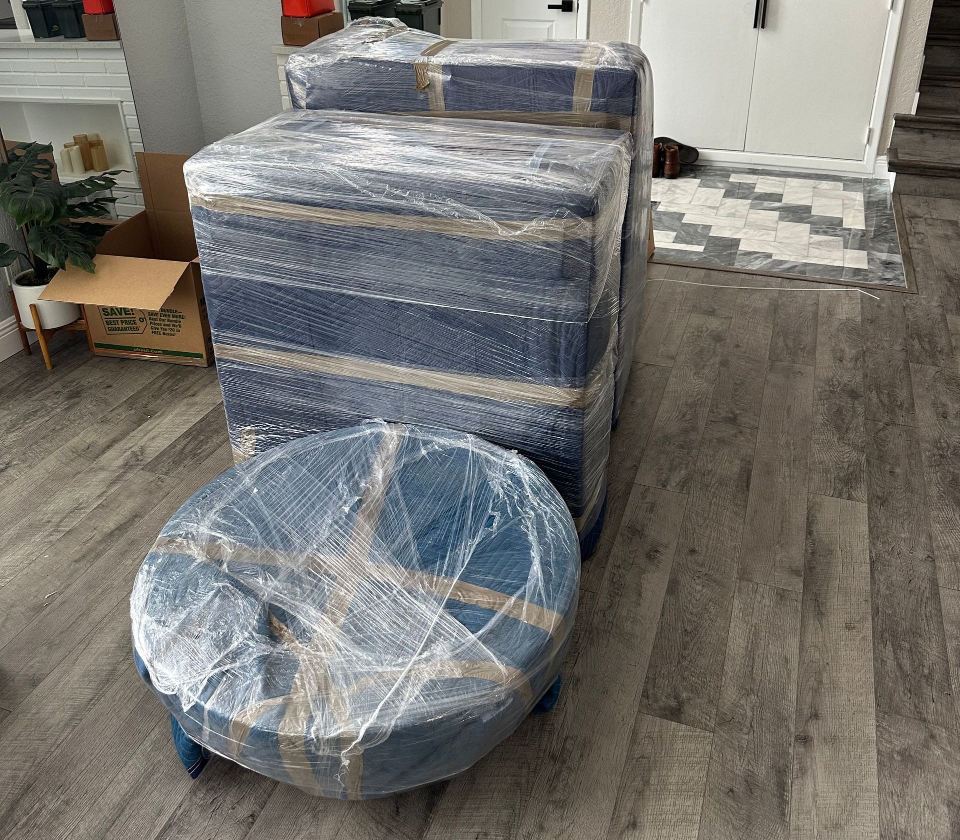 A living room filled with boxes and a round ottoman wrapped in plastic.