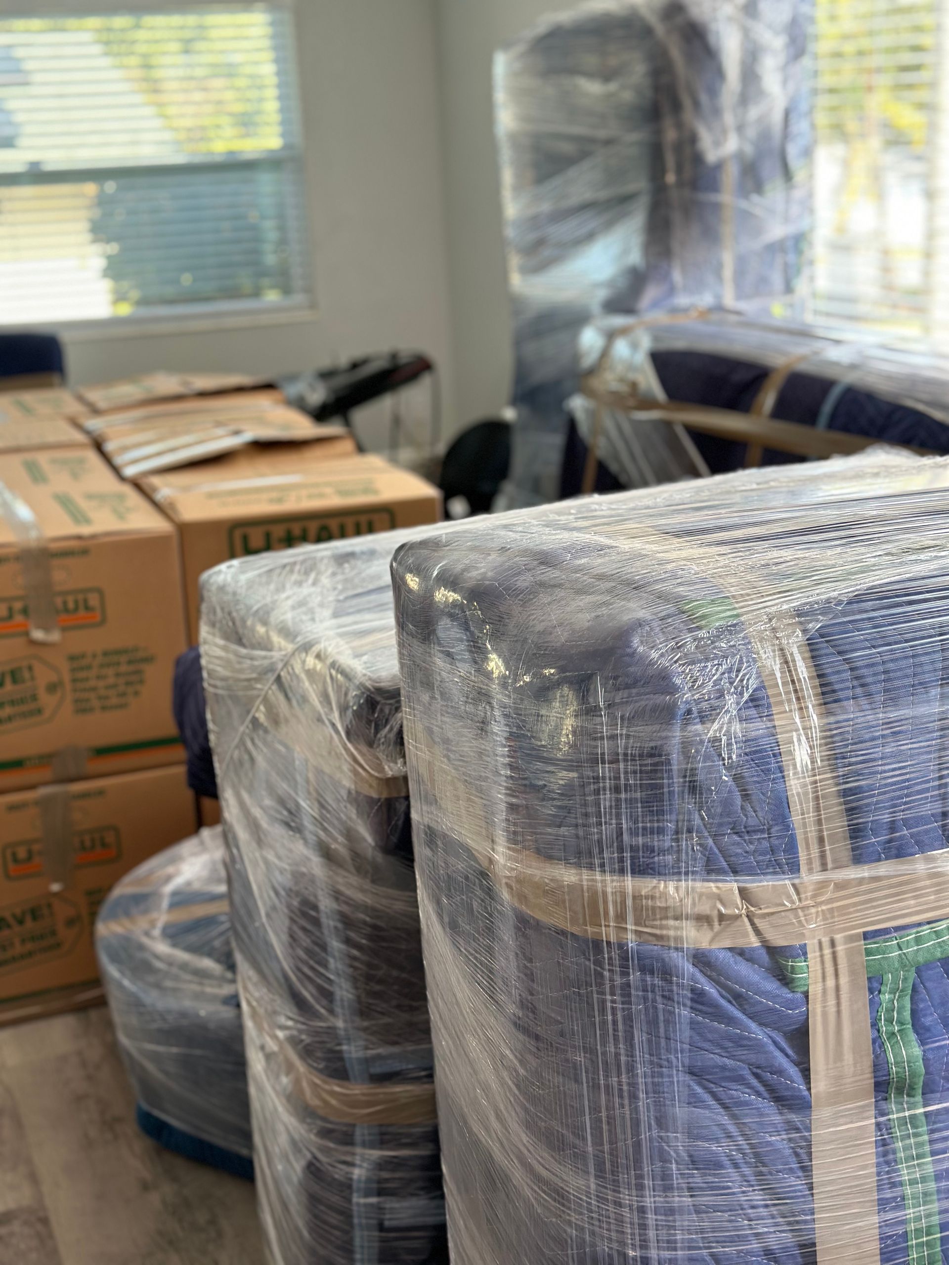 A room filled with boxes and moving blankets wrapped in plastic.