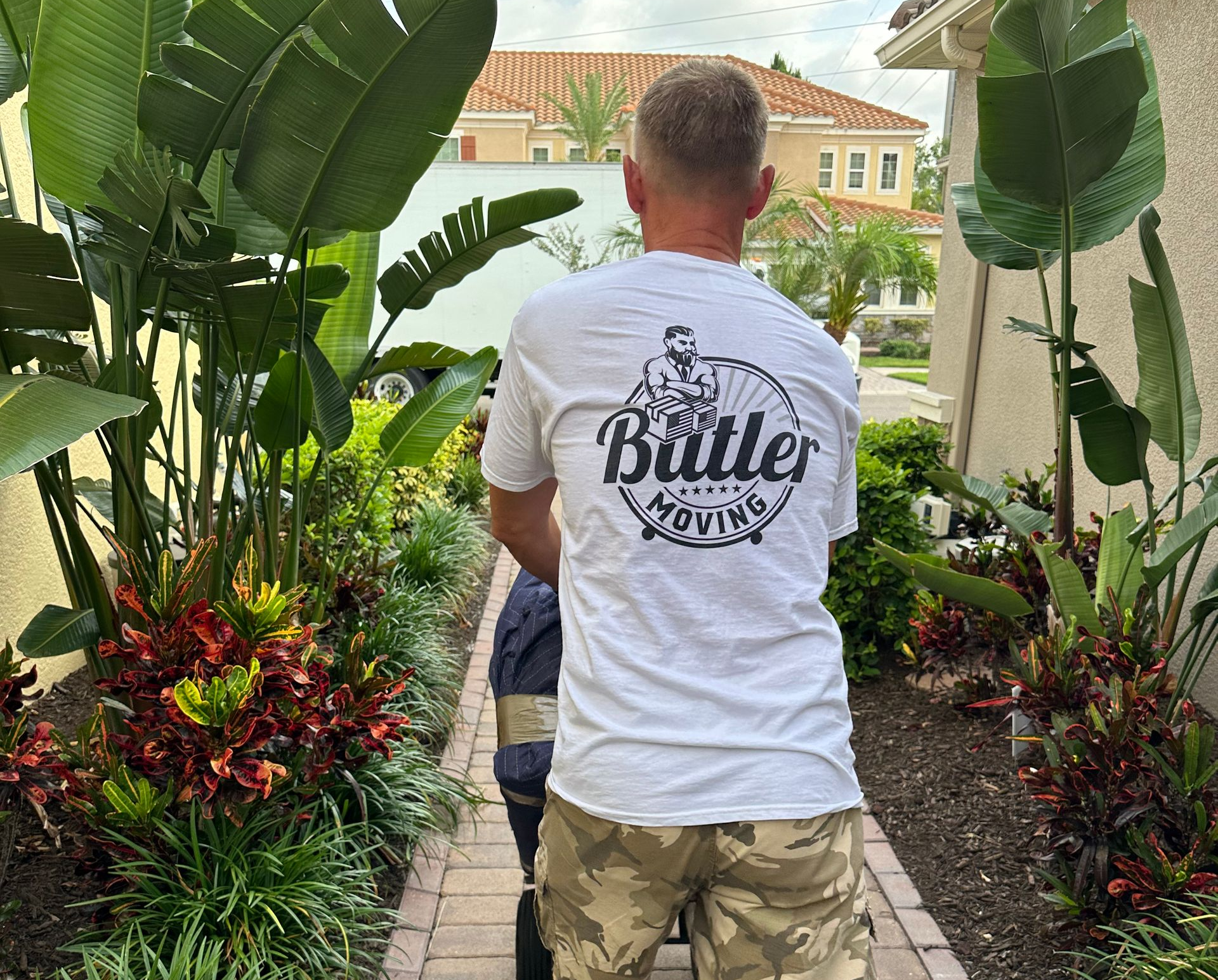 A man in a white t-shirt is pushing a stroller down a brick path.