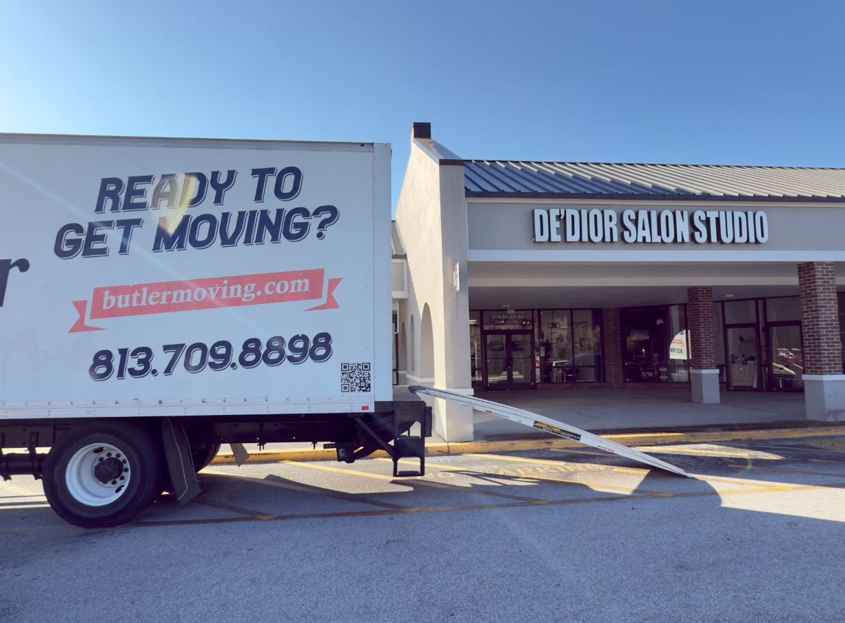 Moving truck parked outside a salon, ramp extended. The truck reads