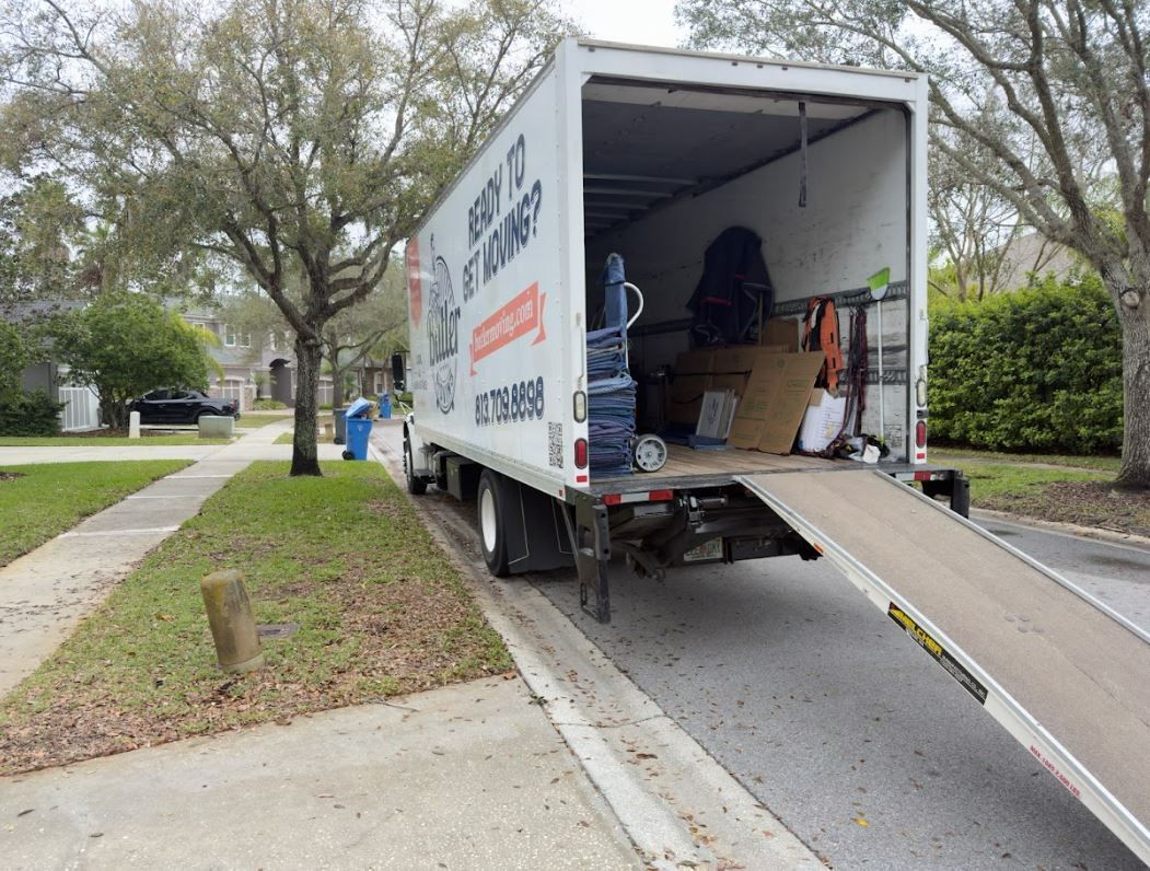 Moving truck parked on a residential street with ramp down; boxes and items inside.