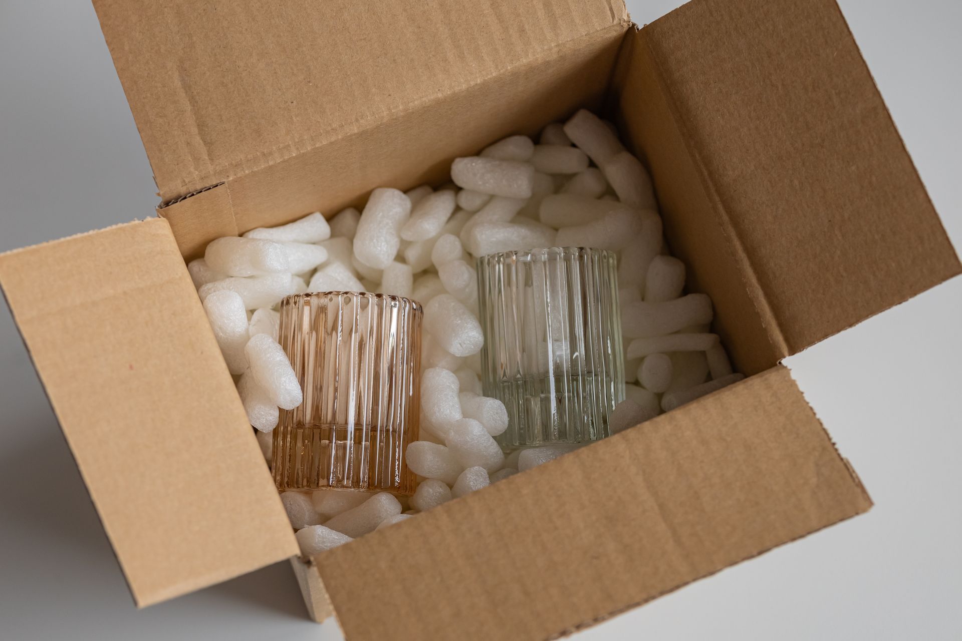 Cardboard box with two glass tumblers nestled in white packing peanuts.