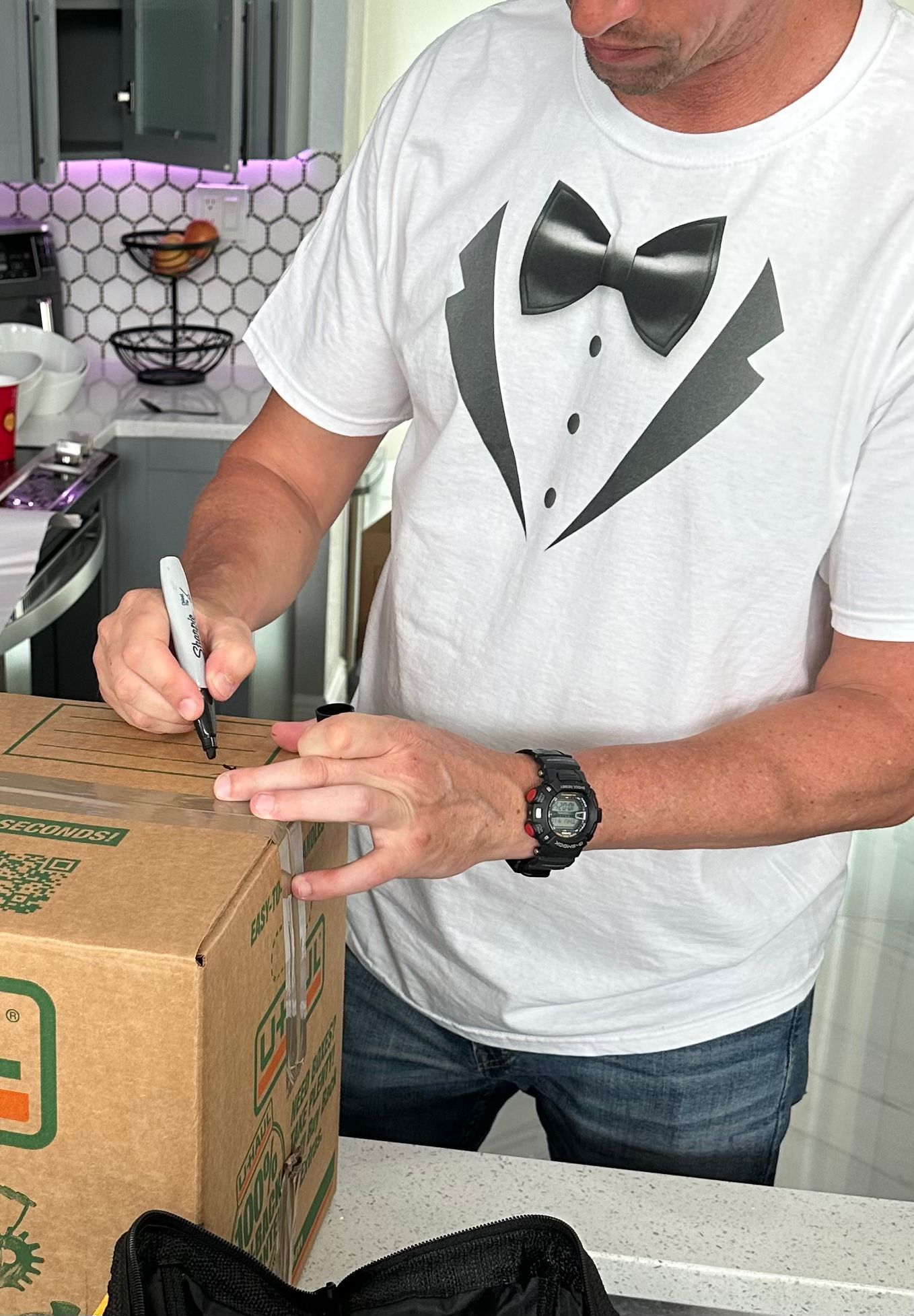 A man wearing a tuxedo shirt is writing on a box