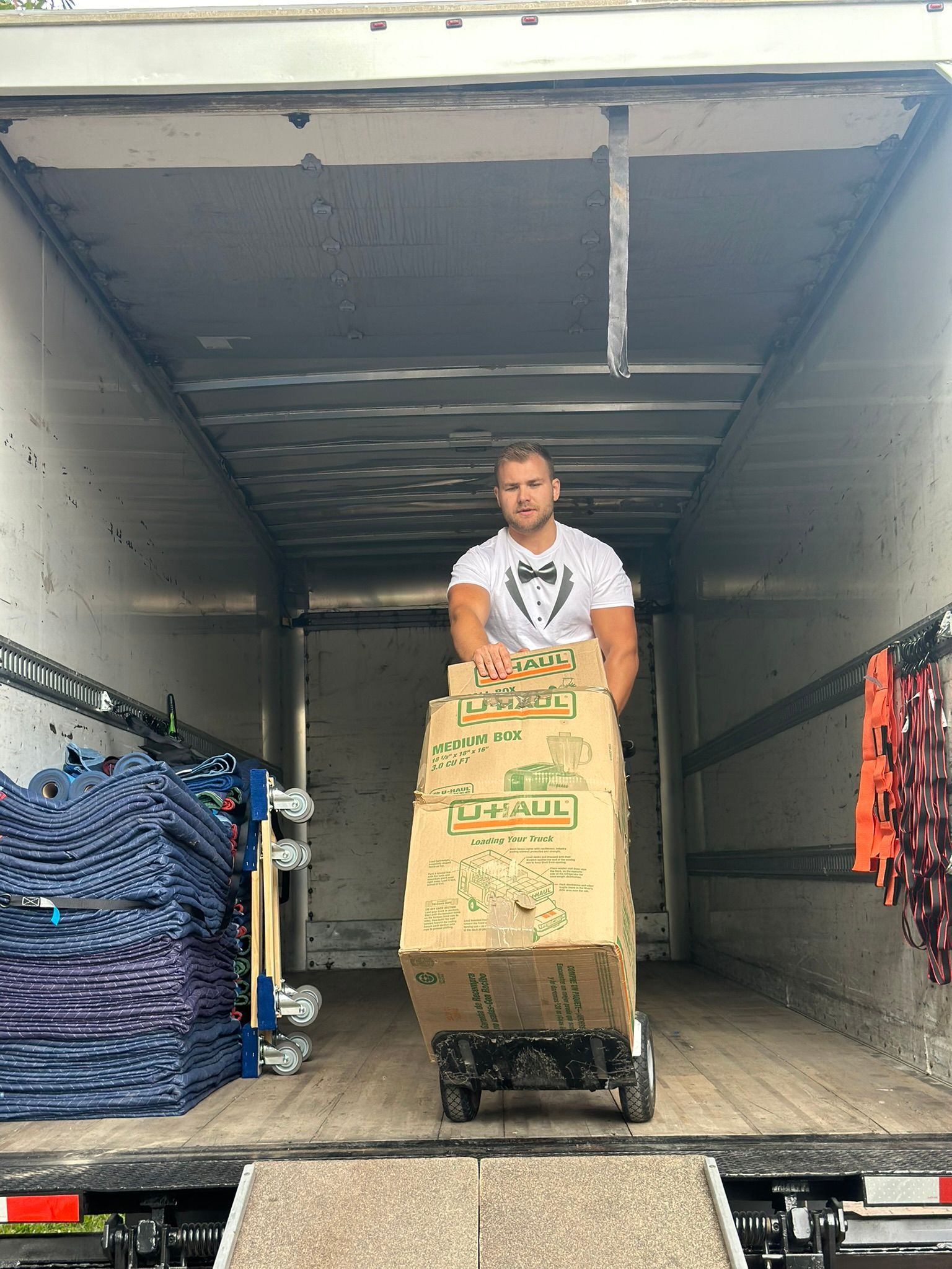 A man is carrying boxes on a dolly in the back of a truck.
