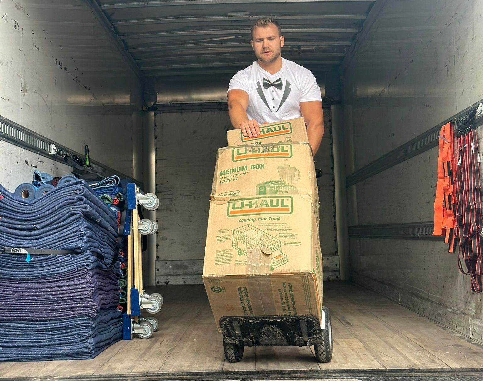 A man is carrying boxes on a dolly in the back of a truck.
