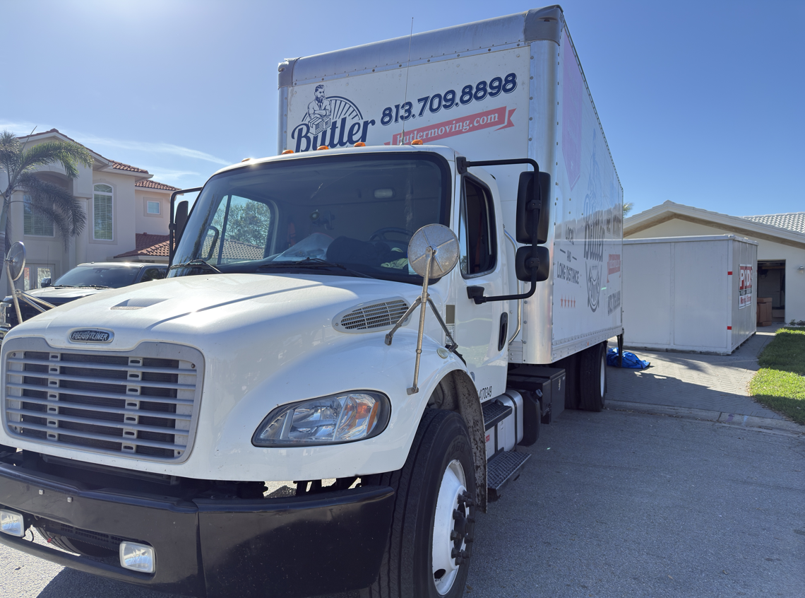 White moving truck parked in a driveway. Building in background, sunny day.