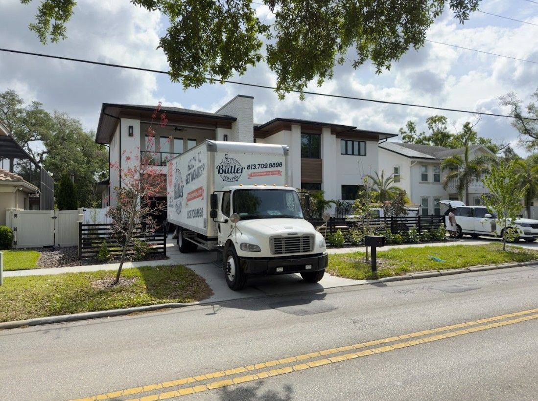 Moving truck parked in front of a modern two-story white house with a landscaped yard; sunny day.