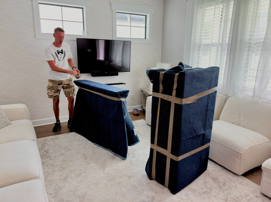 Man in shorts wrapping furniture in a living room, ready for moving.